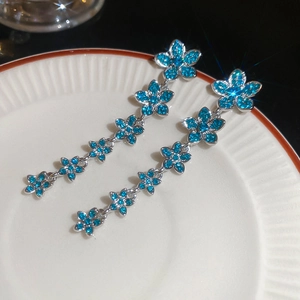 Close-up of elegant long tassel earrings with blue crystals and flower-shaped links