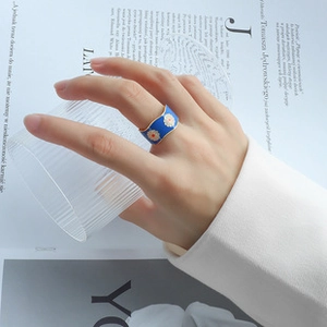Detailed view of a wide blue enamel ring with floral patterns worn by a model