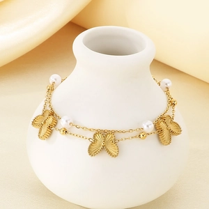 Double-layer gold butterfly chain bracelet with white pearls on a white ceramic display