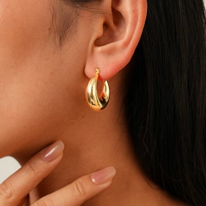 Close-up of model wearing chunky golden teardrop hoop earrings with high-shine metal finish