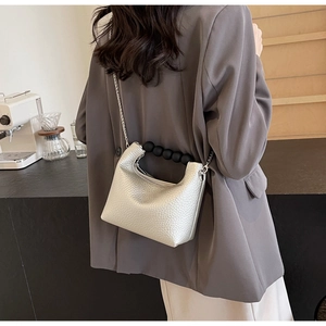 Detail of silver lychee grain crossbody bag with black spherical handle and metal chain