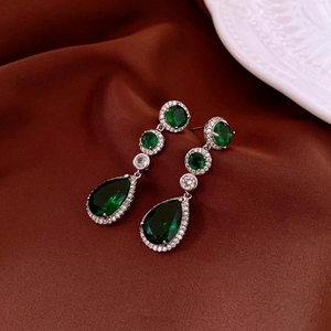 Detailed close-up of water drop earrings with green emerald stones on silk fabric