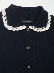 Close-up of dark blue knit cardigan featuring a white crochet lace collar and buttons