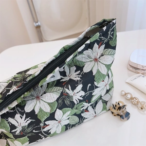 Close-up of floral jacquard makeup bag with white flowers and green leaves on black fabric