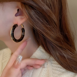 Detail of tortoiseshell resin hoop earring with gold metal trim worn by a model