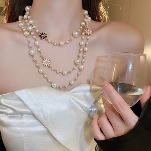 Detail of layered gold necklace with white pearls and elegant flower pendants