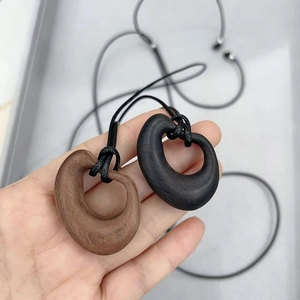 Detail of hand holding oval wooden ring pendants in brown and black with black cords