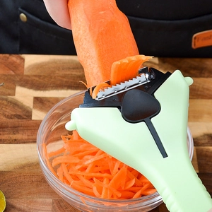 Green 3-in-1 stainless steel fruit peeler shredding carrots into a glass bowl