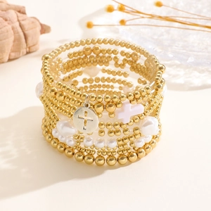 Dettaglio di bracciali multistrato con perle dorate e un ciondolo a forma di croce decorativo