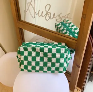 Close-up of green and white checkered knit pouch with metal zipper on a white stand