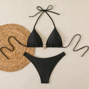 Flat lay of a black two-piece bikini with a gold starfish charm on a woven beach mat