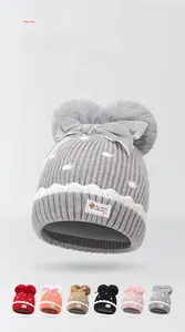 Detail of warm knit baby hat with twin faux fur pom-poms and velvet bow accent