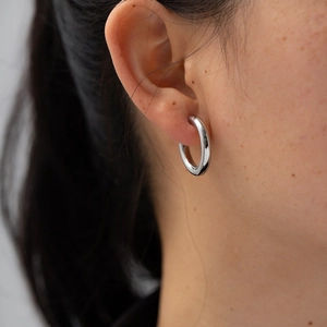 Close-up of thick silver stainless steel hoop earring worn by a model in a minimalist style