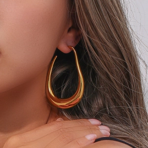 Close-up of a large gold hollow teardrop hoop earring worn by a model in soft light