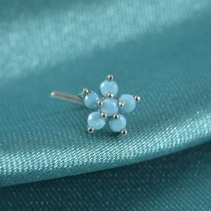 Macro shot of silver flower nose stud with blue stones on teal silk fabric background