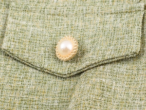 Close-up of green tweed fabric with a pearl and gold chain button on the pocket flap