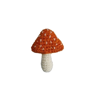 Handmade crochet mushroom brooch with orange spotted cap and cream stem on white background