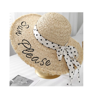 Close-up of raffia sun hat with black Sun Please embroidery and polka dot ribbon bow