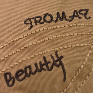 Détail de la broderie 'beauty' marron foncé sur le tissu en toile beige de la casquette
