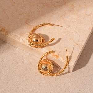 Detail of gold spiral hoop earrings with mirror-polished beads on a stone surface