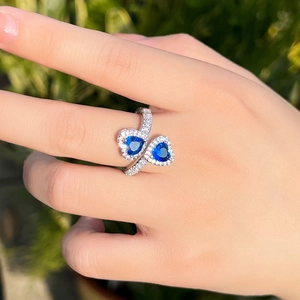 Macro shot of a silver open ring with dual blue heart gemstones and pavé zircon accents