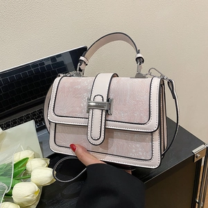 Detail of elegant jacquard handbag with metal H clasp and leather handle on a desk