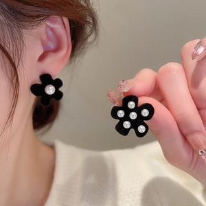 Close-up of black velvet flower earrings with pearl details on model ear and hand