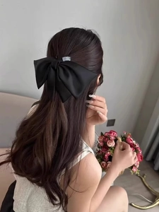 Detail showing an oversized black satin bow hair claw clip styled on wavy hair