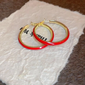 Close-up of geometric red and gold hoop earrings on a textured cream background