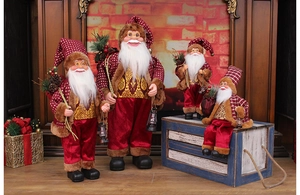 Standing Santa Claus figures in red and gold outfits displayed by a cozy fireplace