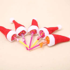 Five lollipop sticks decorated with mini red and white felt Christmas hats on beige background