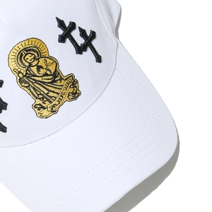 Close-up of golden San Judas Tadeo embroidery and gothic crosses on white baseball cap