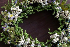 Macro shot of faux berry wreath with mixed green, white and purple berries on wood surface
