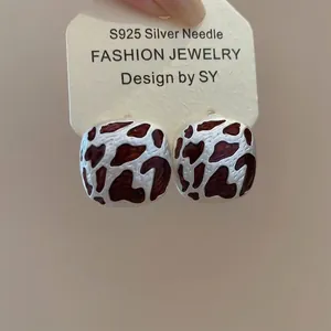 Close-up of S925 silver stud earrings with geometric brown cow pattern enamel detail