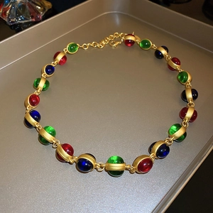 Détail d'un collier vintage doré avec cristaux colorés sur un plateau métallique