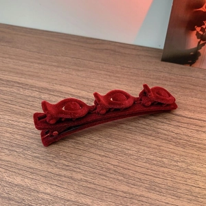 Close-up of red velvet hair clip with three decorative flowers on a wooden surface