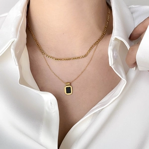 Close-up of layered gold necklace featuring a black onyx geometric square pendant on silk