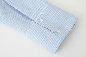 Detailed close-up of striped blue cotton shirt cuff with white lace trim and double buttons