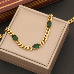 Detail of gold-plated Cuban link bracelet featuring three oval emerald green gemstones