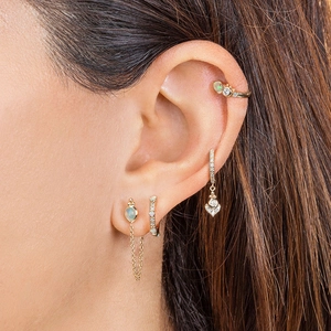 Macro shot of gold earrings set with opal and diamonds on model ear with blurred hair