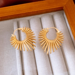Close-up of golden sunburst textured hoop earrings on premium gray velvet display
