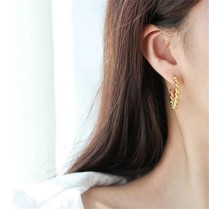 Close-up of gold-plated C-shape twisted hoop earrings worn by a model for a luxury look