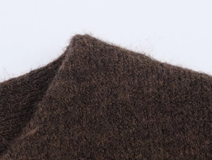 Macro shot of dark brown knitted fabric texture with soft faux fur finish on a grey background