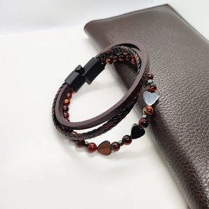 Dettaglio di un bracciale multistrato in pelle intrecciata con perle occhio di tigre e cuore