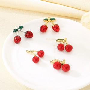 Detail of red cherry charms with gold and silver stems on a white ceramic plate