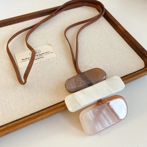 Close-up of tricolor resin rectangle pendant on long necklace over a wooden tray