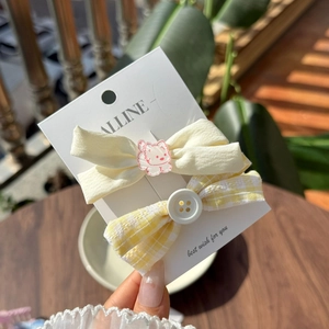 Close-up of cream bow hairpin with pink cat and yellow plaid bow with button on a card