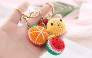 Close-up of handmade crochet fruit charms including orange and watermelon on gold keychain