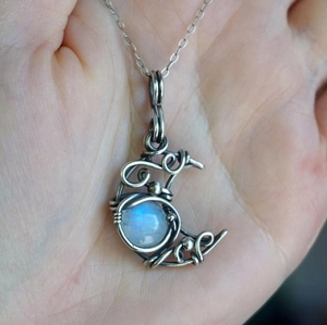 Detail of silver wire-wrapped moon pendant with iridescent moonstone on a necklace
