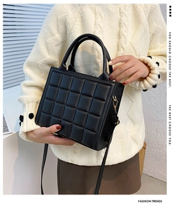 Detail of black quilted leather crossbody bag with padded handles and fine stitching